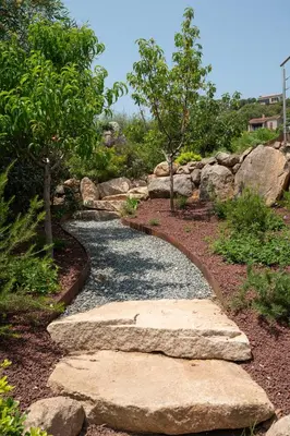 a stone path in a garden with rocks and trees at Villa avec piscine et vue mer à 230m de la plage in Zonza