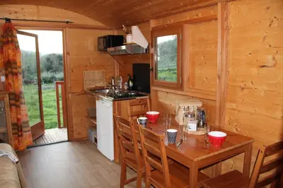 a dining room with a table and a kitchen in a cabin at Le nid des crinières vagabondes in Oletta