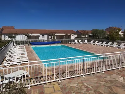 a swimming pool with chairs and a fence at Mini villa T2, 200 m de la plage, piscine chauffée, jardin in Prunete