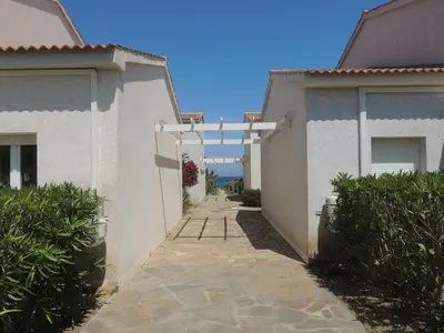 a walkway between two white buildings with bushes at Mini villa T2, 200 m de la plage, piscine chauffée, jardin in Prunete