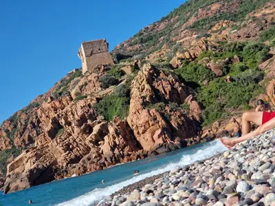 a person standing on a rocky beach with a castle on a mountain at T2 vue mer & montagne Golfe de Porto-Ota in Porto Ota