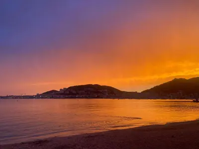 a sunset on the beach with a city in the background at Appartement pieds dans l eau in Ajaccio