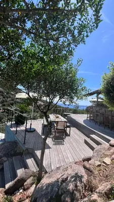 a wooden deck with a table and a tree at Secluded Villa With Sea View In Palombaggia in Porto-Vecchio