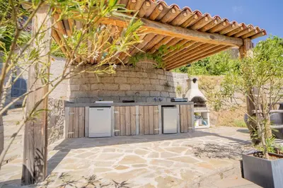 an outdoor kitchen in a patio with a wooden pergola at Sud-corse bavella location montagne et mer in Sorbollano