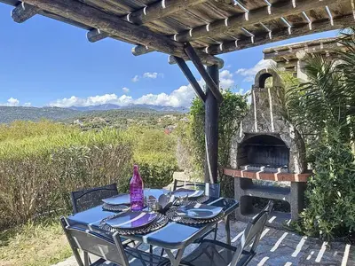 a table and chairs on a patio with an outdoor oven at Mini Villa Santa Giulia double vue mer à 5 min de la plage à pied in Porto-Vecchio