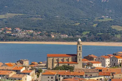 a town with a clock tower next to a body of water at monte barbatu in Propriano