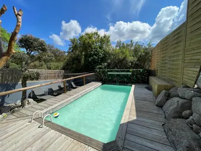 a swimming pool on a wooden deck next to a house at Appartement avec piscine 8 personnes in Porto-Vecchio