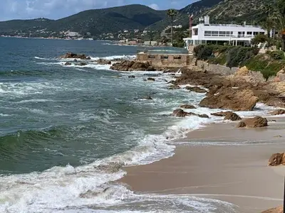 a beach with a building and the ocean with waves at Coin de paradis aux Sanguinaires in Ajaccio