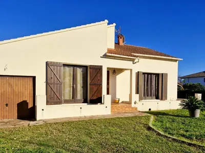 a white house with brown doors and a yard at Villa à quelques pas de la plage in Santa-Lucia-di-Moriani