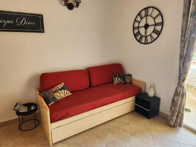 a red couch in a room with a clock on the wall at linguizzetta , les marines de bravone in Linguizzetta