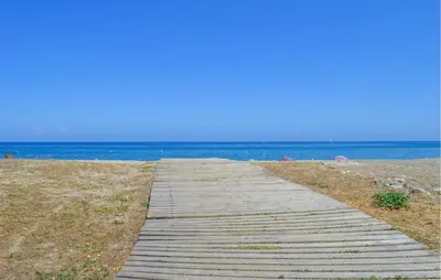 a wooden path to the beach with the ocean in the background at Villa Plage À Pieds in Moriani Plage