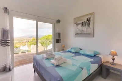 a bedroom with a large bed and a large window at Padulaccia by Pinarello Villa Services in Pinarellu