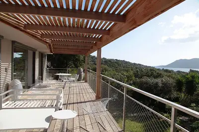a wooden deck with chairs and a table on a balcony at Villa Alta Vista in Porto-Vecchio