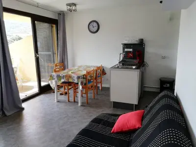 a living room with a table and a kitchen with a clock at T2 log entier Porticcio 35m piscine-mer-resto 400m in Grosseto-Prugna