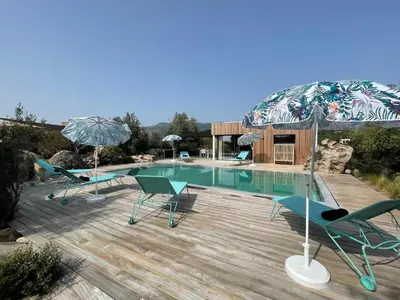 a pool with chairs and an umbrella on a wooden deck at luxe et sérénité in Lecci