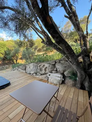 a table and chairs on a wooden deck with a tree at Lodge sous les oliviers in Propriano