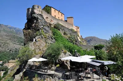 a castle on top of a mountain with tables and umbrellas at Charmant studio avec extérieur in Corte