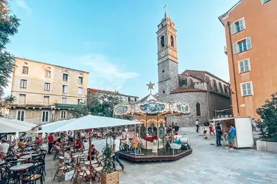 a group of people sitting at tables in a street with a clock tower at Appartement T2 à Porto-Vecchio in Porto-Vecchio