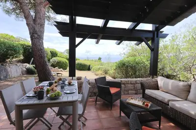 a patio with a table and chairs and a couch at Sous le Pin - Villa paisible face aux îles Lavezzi in Bonifacio