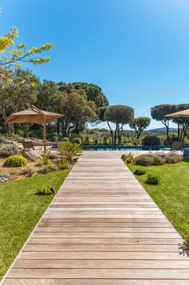 a wooden path leading to a pool with an umbrella at Villa Alba Di Pinarello in Pinarellu