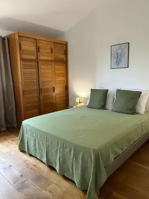 a bedroom with a green bed with a wooden cabinet at T2 dans villa avec piscine in Porto-Vecchio