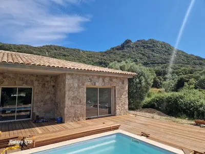a house with a wooden deck and a swimming pool at Charming stone villa with pool in Figari