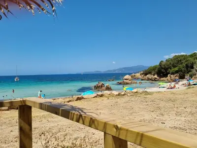 a beach with people in the water and a wooden fence at Appartement Neuf Grande Terrasse AGOSTA PLAGE in Albitreccia