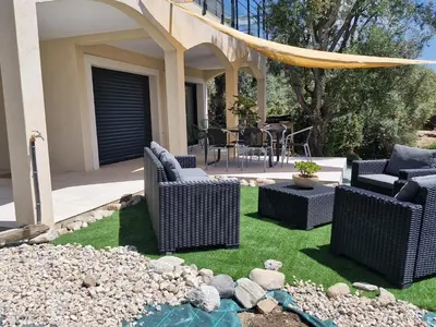 a patio with wicker chairs and a table on grass at Maison Rez-de-jardin 80 m de la plage in Serra-di-Ferro