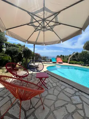 a patio with chairs and an umbrella next to a pool at villa vue mer avec piscine et jardin arboré in Coggia
