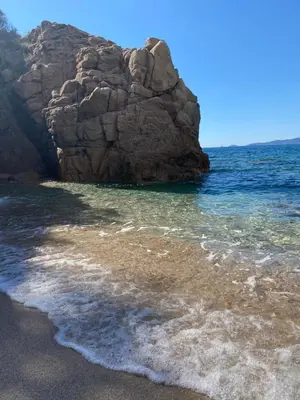 a beach with a large rock in the ocean at appartement T2 rive sud porticcio vue mer in Pietrosella