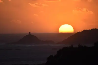 a sunset over the ocean with a lighthouse on a hill at Briloc Appartements Pietrosella à 50m de la plage in Pietrosella