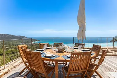 a dining table with chairs and a view of the ocean at Villa Lume Di Palombaggia in Musoleu