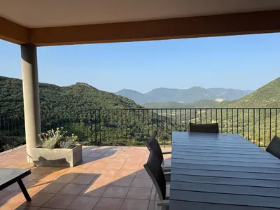 a deck with a table and chairs and mountains at Gîte Inseme, le calme entre mer et montagne en Corse in Arbellara