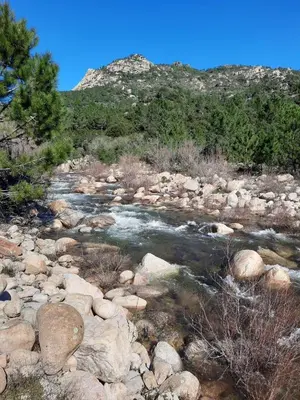 a river with rocks and trees and a mountain at Clos Jeannette Villa près de la plage de Pinarelle et des piscines naturelles du Cavu in Zonza