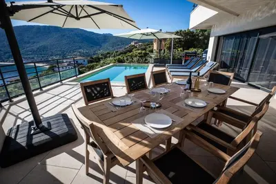 a wooden table with chairs and an umbrella on a patio at Villa d'architecte classée 5 étoiles in Campomoro