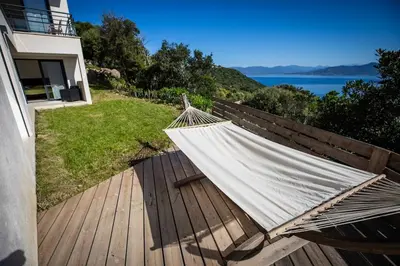 a hammock on a deck with a view of the water at Villa d'architecte classée 5 étoiles in Campomoro