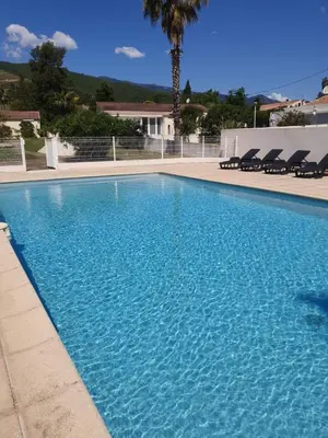 a large blue swimming pool with chairs in front of a house at T2 climatisé avec piscine in Prunelli-di-Fiumorbo