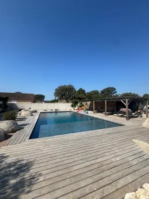 a swimming pool next to a wooden deck at Villa Domaine U Murtonu in Porto-Vecchio