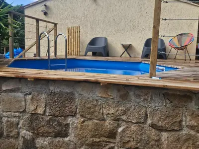 a swimming pool with a stone wall and a wooden deck at Maison au coeur du maquis in Porto-Vecchio