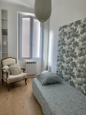 a bedroom with a bed and a chair and a window at Au coeur de Sartène appartement de charme dans un écrin de verdure in Sartène
