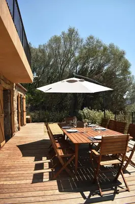 a wooden table with a white umbrella on a deck at Bergerie avec piscine chauffée Sotta in Sotta
