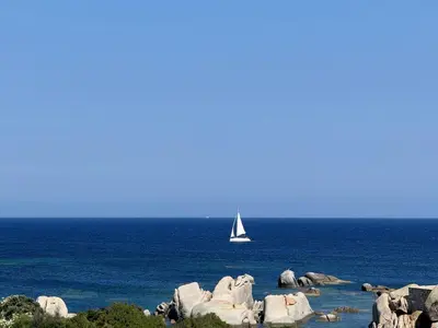 a sail boat in the ocean with rocks and water at B&B Les Capitaineries in Bonifacio