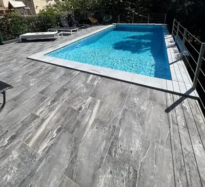 a swimming pool with a wooden floor and blue water at APPARTEMENT 2 CHAMBRES PISCINE A PARATGEr in Porto-Vecchio