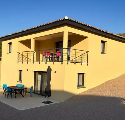 a yellow house with a balcony with chairs and a table at 2 logements a porto vecchio in Porto-Vecchio