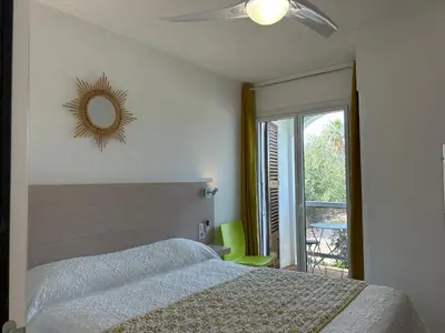 a bedroom with a bed with a ceiling fan and a mirror at Hôtel Punta e Mare des Chambres ou des Appartements T2 in Cargèse