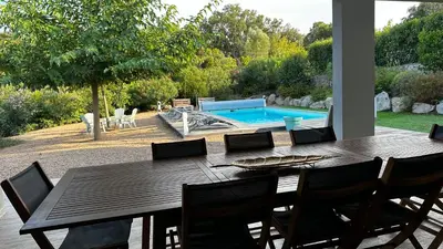a wooden table with chairs and a swimming pool at Domaine LOADANA in Sainte-Lucie de Porto-Vecchio