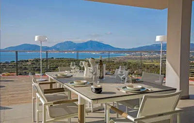 a dining table with white chairs and a view of the ocean at Villa Clémentines Porticcio in Grosseto-Prugna