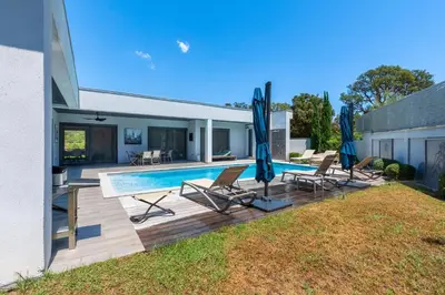 a pool with chairs and umbrellas in a yard at La Villa Grazzoso - Piscine Privée in Sainte-Lucie de Porto-Vecchio