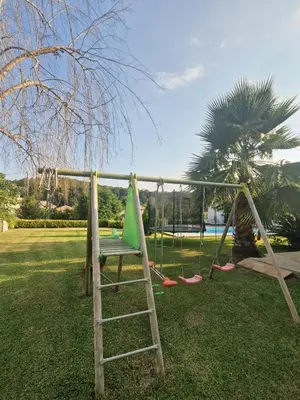 a swing set in a park with a palm tree at Logement indépendant avec piscine privée in Penta-di-Casinca