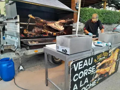 a man cooking meat on a grill next to a truck at U PINU Appartement 3 chambres in Olmeto